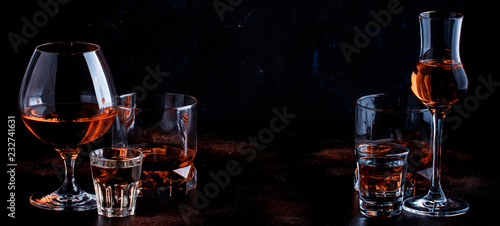 Selection of strong alcoholic drinks in glasses and shot glass in assortent: vodka, rum, cognac, tequila, brandy and whiskey. Dark vintage background, selective focus, copy space
