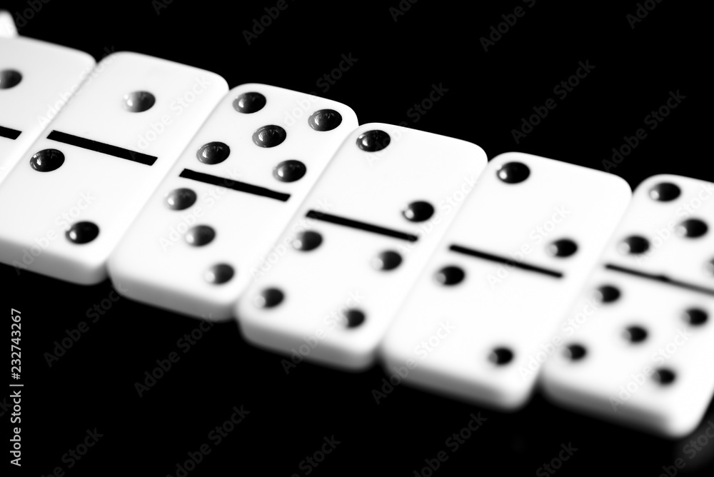 Dominoes are scattered on a dark surface close up. Black and white Dominoes are scattered on a dark surface close up. Black and white