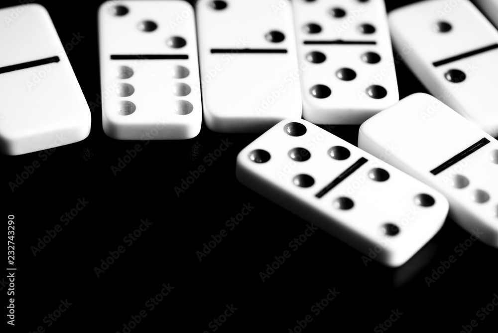 Dominoes are scattered on a dark surface close up. Black and white Dominoes are scattered on a dark surface close up. Black and white