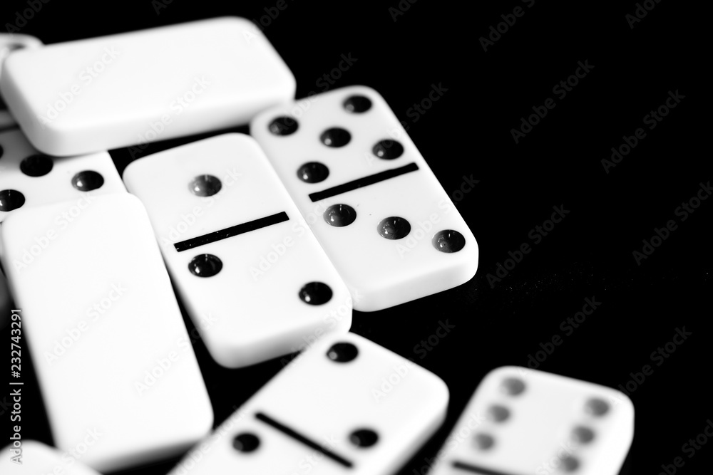 Dominoes are scattered on a dark surface close up. Black and white Dominoes are scattered on a dark surface close up. Black and white