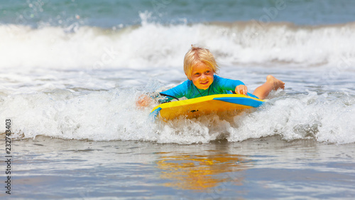 Photography Happy baby boy - young surfer ride on surfboard with fun on sea waves