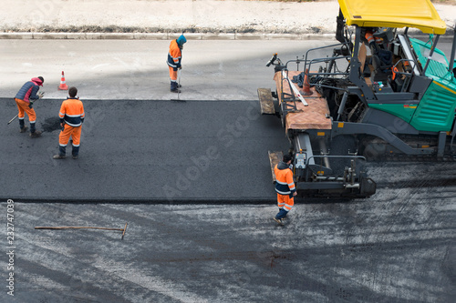 Asphalt paver machine and road construction workers on the road repair site. Road renewal process, construction working. High angle view photo