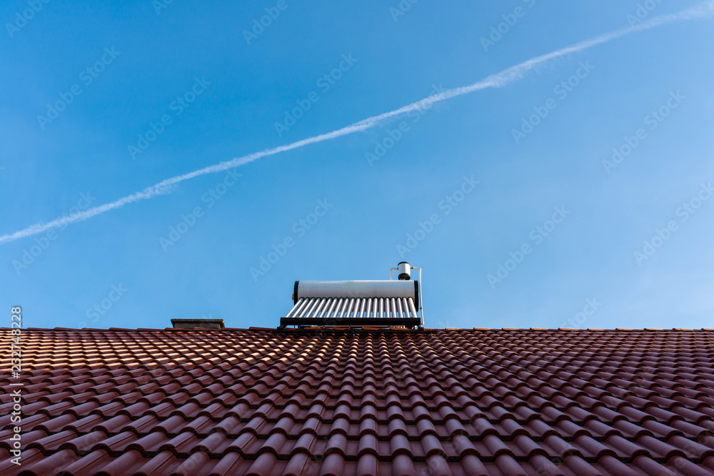 Frozen solar water heater boiler on rooftop, passing aeroplane, blue sky background. Frozen solar water heater boiler on rooftop, passing aeroplane, blue sky background.