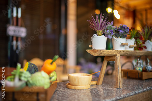 Dining room decorated with synthetic plastic fruit and small cactus flower on wooden table with blurred background.