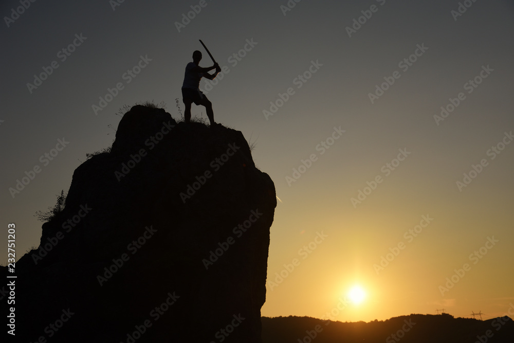 Silhouette of a man with katana exercising on edge of the cliff