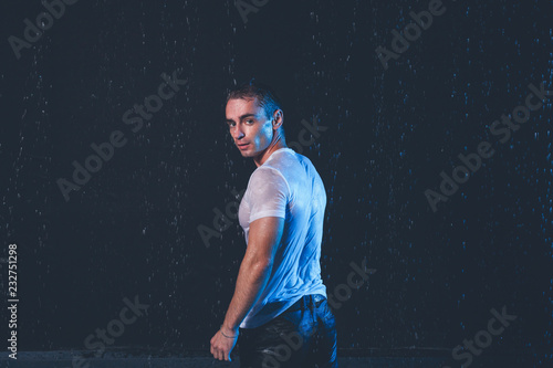 Fresh portrait of muscular man with water splashes on dark background.