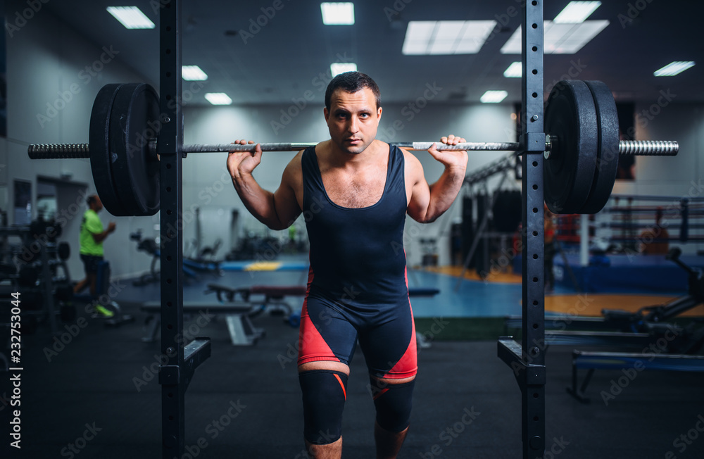 Muscular athlete poses at the stand with barbell Muscular athlete poses at the stand with barbell