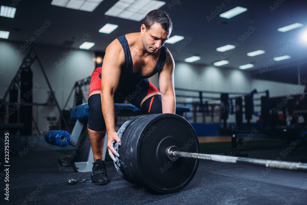 Male powerlifter prepares a barbell in gym
