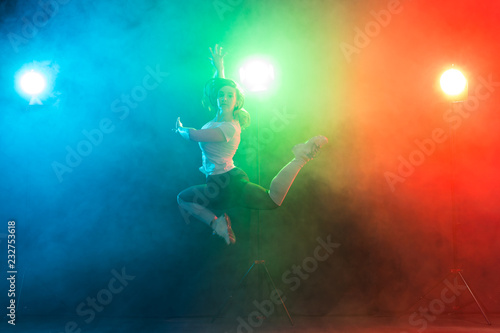 Dancing, sport, jazz funk and people concept - young woman jump in the darkness under colourful light