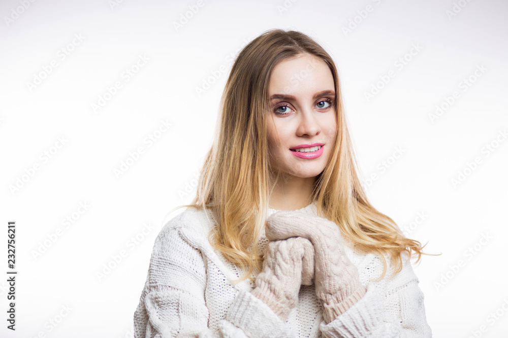 Happy cheerful young woman wearing knitted warm beige sweater and mittens and looks at camera on white background Happy cheerful young woman wearing knitted warm beige sweater and mittens and looks at camera on white background