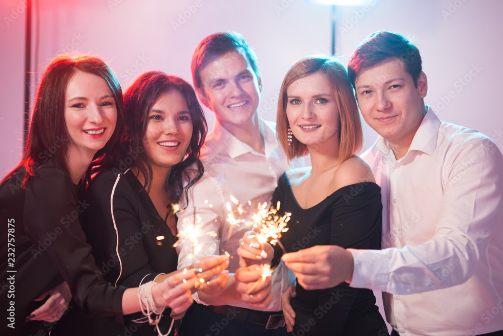 Celebrating with fun. Group of cheerful young men and women carrying sparklers. New year, holidays and party concept.