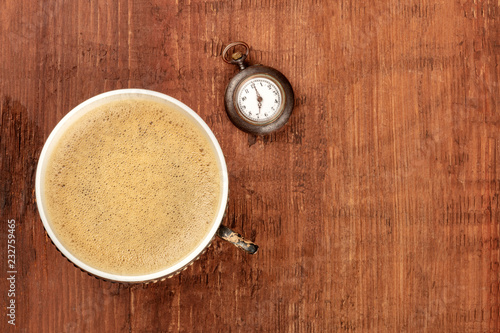 Coffee Time, vintage style. An overhead photo of coffee in a retro cup, shot from above on a dark rustic wooden background with an old watch and a place for text