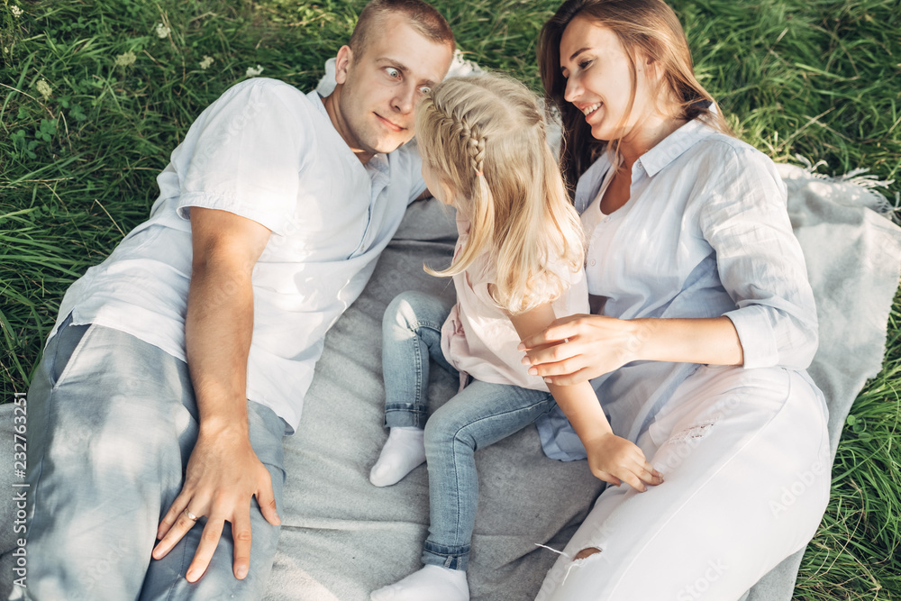 Young Adult Couple with Their Little Daughter Having Fun in the Park Outside the City, Family Weekend Picnic Concept, Three People Enjoying Summer Time