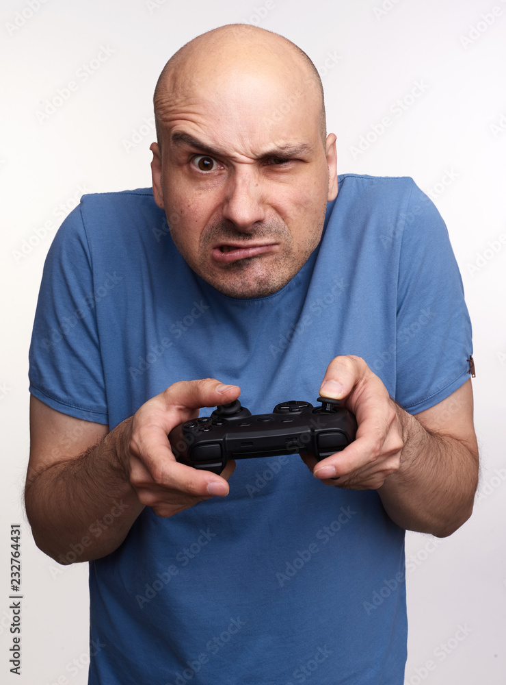 Angry bald man plays computer game isolated on grey studio background