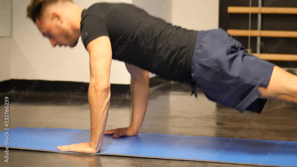 Attractive muscular young man in gym working out, doing exercises for pecs, push-ups, on the ground on a mat Attractive muscular young man in gym working out, doing exercises for pecs, push-ups, on the ground on a mat