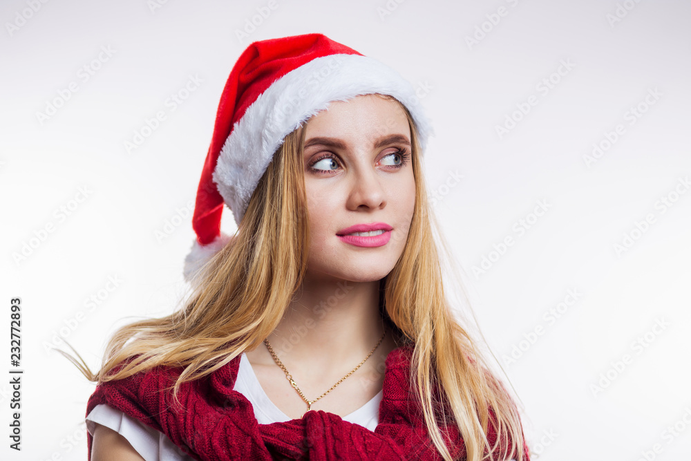 Close-up portrait of young dreaming blonde woman wearing red Santa hat and sweater on white background Close-up portrait of young dreaming blonde woman wearing red Santa hat and sweater on white background