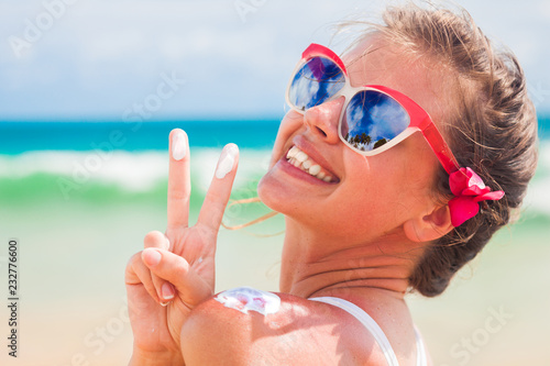 Close up of young woman in sunglasses putting sun cream on shoulder