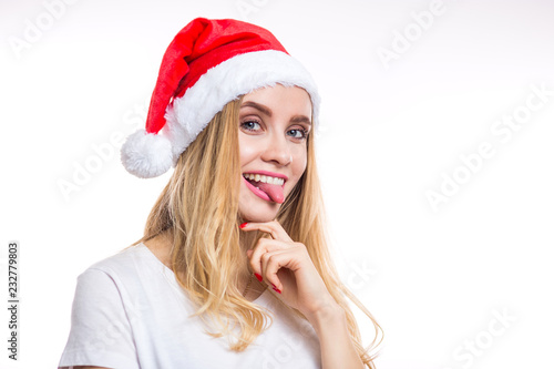 Funny cheerful smiling blonde woman wears a red Santa hat and shows her tongue to the camera on a white background