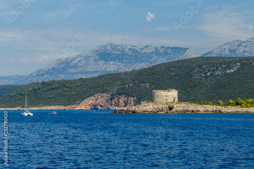 Stony seashore, mountains on the horizon and the old round fortress
