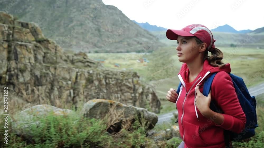Traveler girl in cap with backpack climbing stones mountains. Close-up view. Background mountains and river. Traveler girl in cap with backpack climbing stones mountains. Close-up view. Background mountains and river.