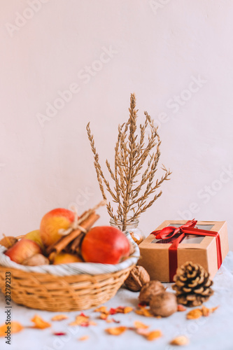 Still life with cinnamon sticks wrapped in twine  cone  apples in a wicker basket stand on a striped linen cloth  walnuts and flower petals in bank. Concept of home comfort in autumn or winter.
