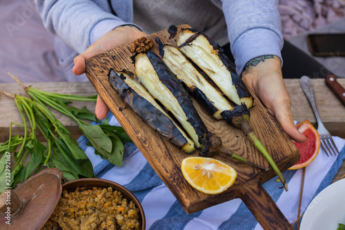 Woman hands holds roasted, grilled, baked eggplants on wooden cutting board. Vegan vegetarian healthy food, paleo diet. Vegetables
