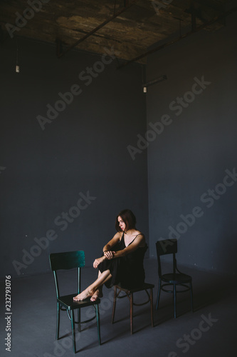 The social theme female loneliness pain suffering. Abastration male violence family. A young beautiful Caucasian woman in black clothes sitting on three chairs in large dark room. Srach and despair photo