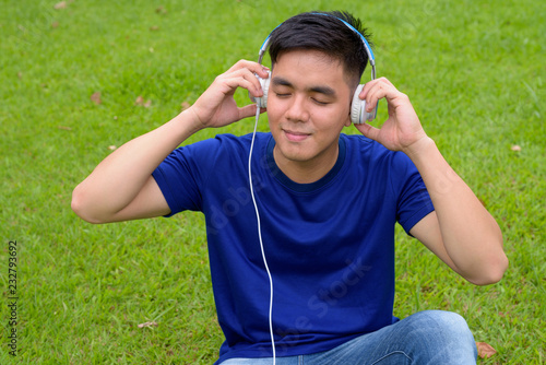 Young handsome Asian man relaxing at the park with headphones
