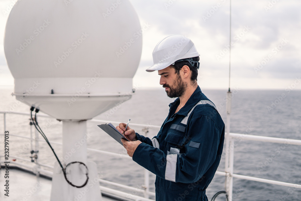 Marine service technician or serviceman near VSAT terminal on deck of vessel or ship. He is filling checklist Marine service technician or serviceman near VSAT terminal on deck of vessel or ship. He is filling checklist