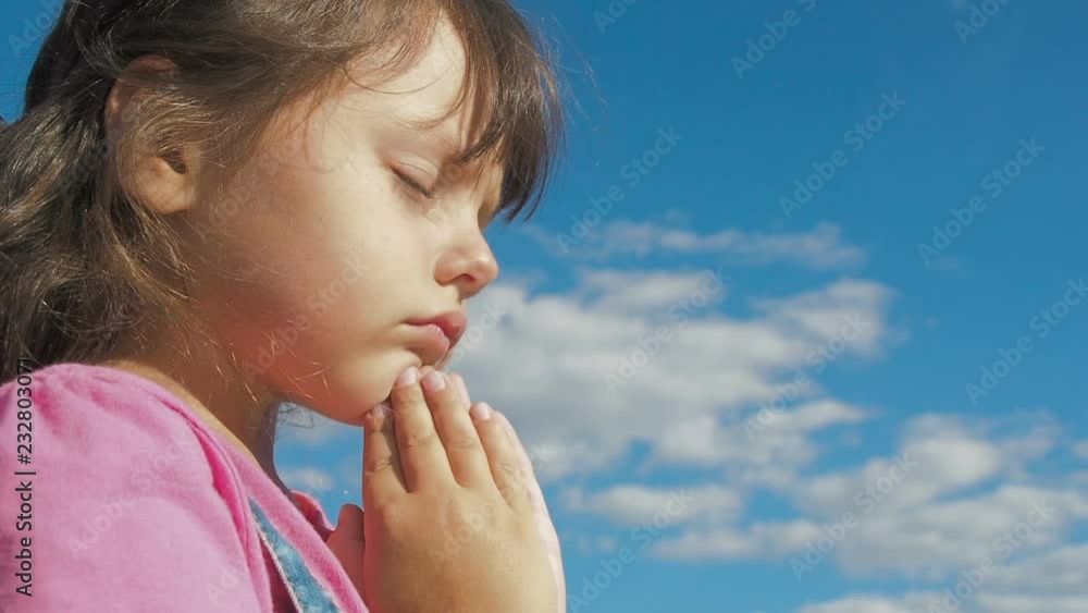 The child is praying. Little girl prays against the sky. The child is praying. Little girl prays against the sky.