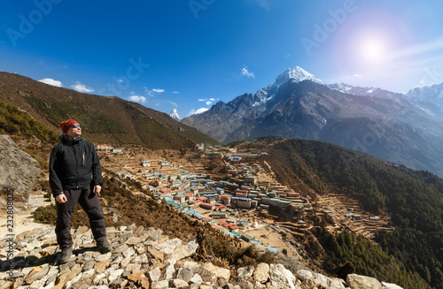 Everest track. Namche Bazaar. The tourist stands on a view poin at sunrise. He's looking at the panorama. Below is the village. The mountains on the horizon.
