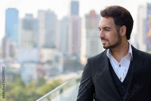 Young handsome Indian businessman thinking at rooftop in Bangkok