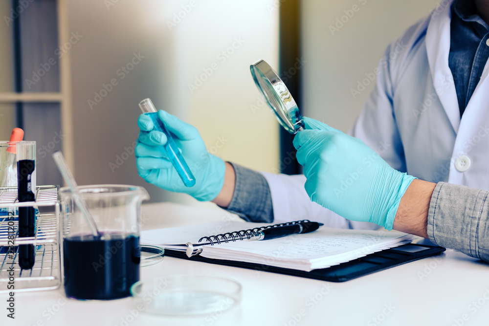 Chemist or scientist using magnifying glass dispense the solution in a glass jar. Chemist or scientist using magnifying glass dispense the solution in a glass jar.