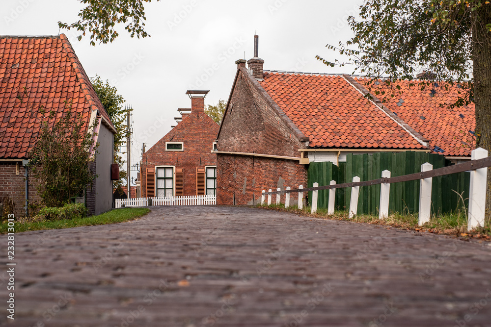 View from approach route over dike on traditional village with farmhouses and old pavements. View from approach route over dike on traditional village with farmhouses and old pavements.