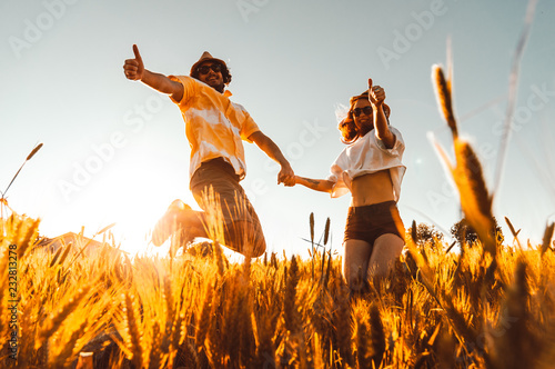 Happy couple having fun jumping on a wheat field at vacation at sunset. Concept about people, love, travel and lifestyle