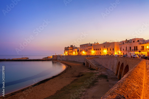 A view of the sea during sunrise in Gallipoli, Italy from the old wall in the city center with the street lights on