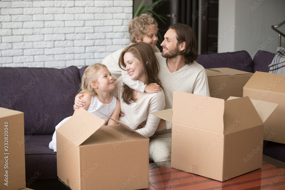 Young family with little children hugging sitting on couch in living room, cardboard boxes. Young first time buyers, parents, preschool kids happy buy new house, real estate. Moving, mortgage concept Young family with little children hugging sitting on couch in living room, cardboard boxes. Young first time buyers, parents, preschool kids happy buy new house, real estate. Moving, mortgage concept