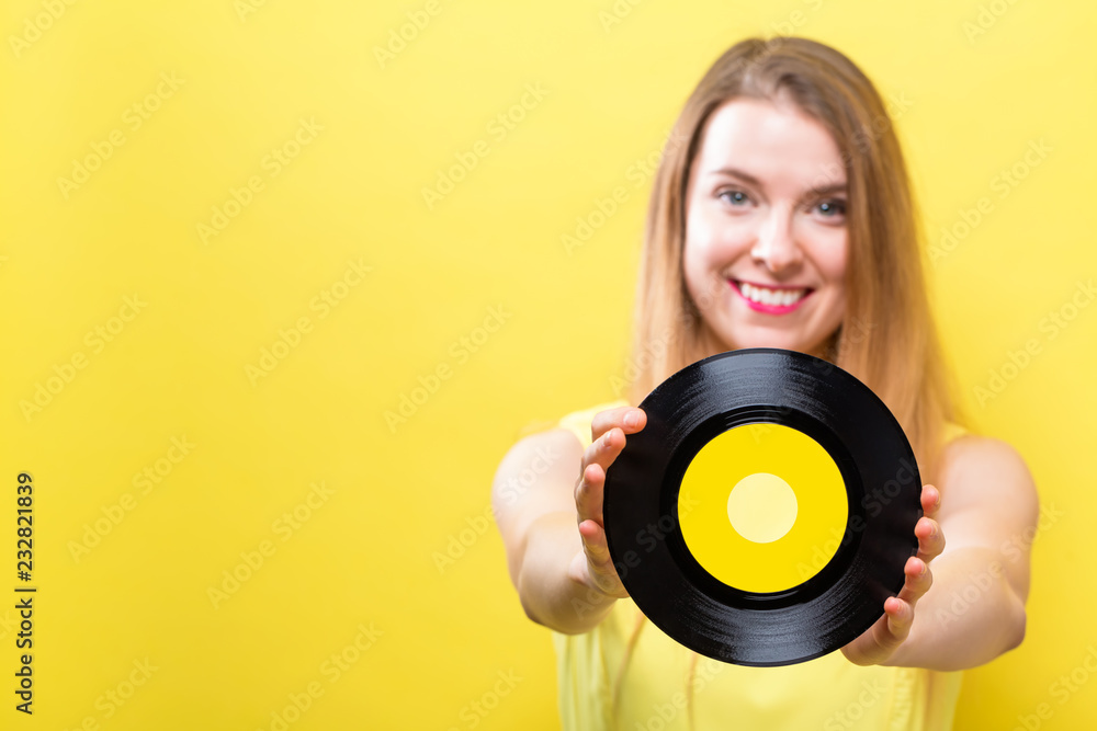 Fototapeta premium Young woman with a vintage vinyl record on a yellow background