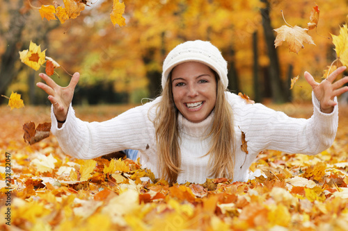 Happy middle age woman throwing yellow autumn leaves