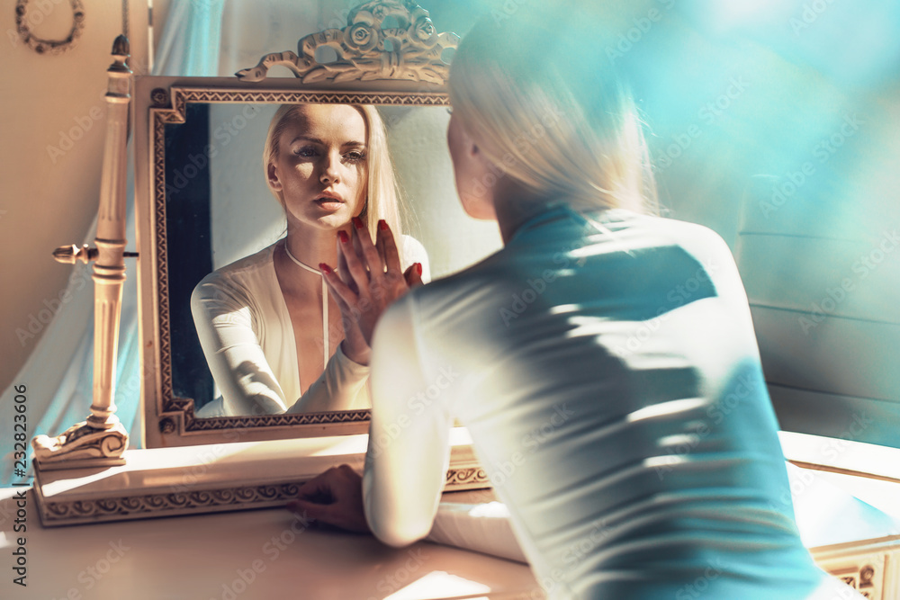 elegant blonde looking at her mirror reflection - obrazy, fototapety, plakaty 
