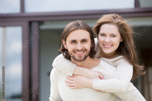 Portrait of attractive smiling married couple outdoors, looking at camera. Close up head shot young positive husband and wife piggyback ride. Happy family and real estate owners or relocation concept © fizkes