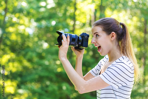 Young woman with a professional digital SLR camera on a bright summer day in the forest
