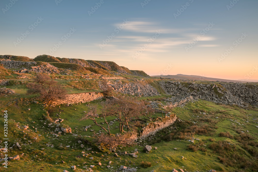 Obraz premium Stunning landscape sunset image over abandoned Foggintor Quarry in Dartmoor with raking soft sunlight over ruins and derelict buildings