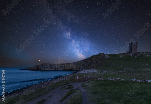 Vibrant Milky Way composite image over landscape of Dunstanburgh Castle on Northumberland coastline in England photo