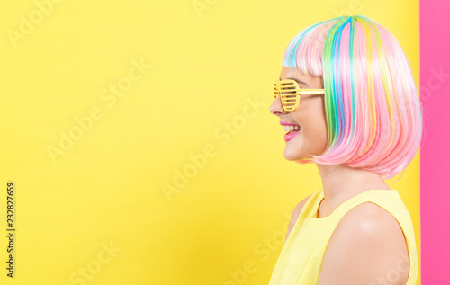 Young woman in a colorful wig with shutter shades sunglasses on a split yellow and pink background © Tierney