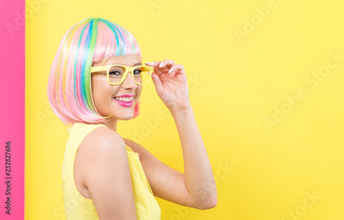 Young woman in a colorful wig with sunglasses on a split yellow and pink background