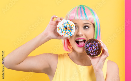 Beautiful woman in a colorful wig with doughnuts on a split yellow and pink background