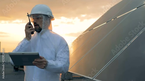 Sunset landscape on a rooftop with a male expert talking on a transmitter beside a solar battery