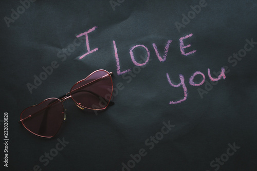 Pink glasses in the shape of a heart on a black mint background. The inscription is pink I love you. Valentine's Day photo