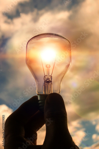 light bulb in the hand of a man against a blue sky with clouds. concept business vision, creativity, business ideas.